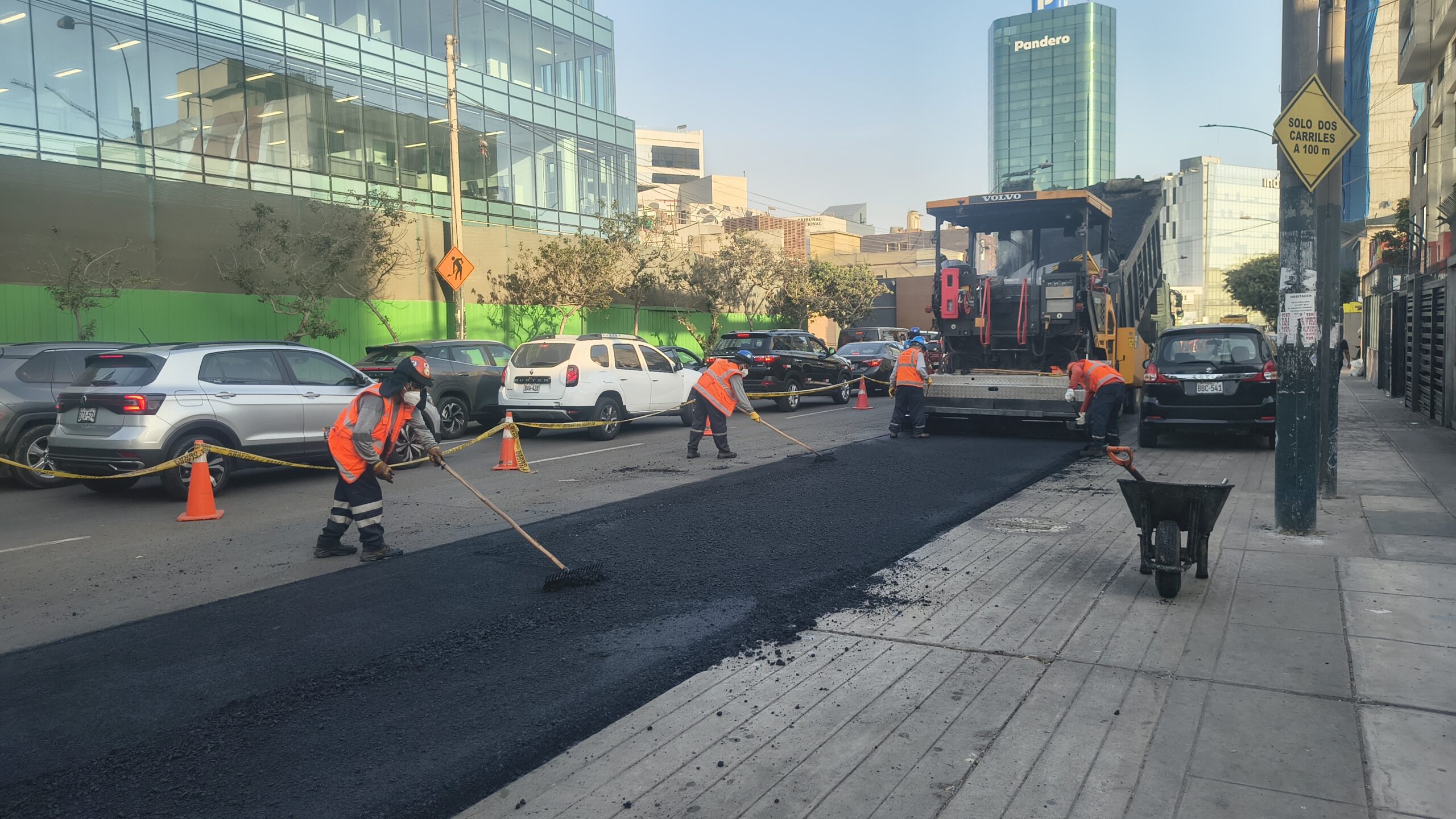 Cuadrilla de Asfaltec Perú pavimentando calle junto a edificio corporativo